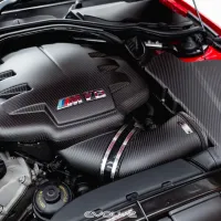 A carbon-fiber engine cover features an "M V8" emblem. The engine is in a clean, organized engine bay within a red sports car. The bottom of the image displays the brand name "EVOLVE."