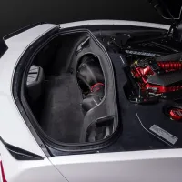 Car trunk with an exposed internal compartment showcasing a red, high-performance engine and carbon fiber components in a black and white vehicle, set against a dark background.