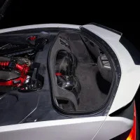 A high-performance car engine with exposed red and black components is shown in the rear compartment of a sleek white sports car, illuminated against a dark backdrop.