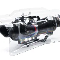 A carbon fiber exhaust pipe encased in a clear plastic protective cover, placed against a white background. The exhaust is mounted to metal brackets visible through the transparent casing.
