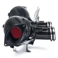 A high-performance air intake system with dual carbon fiber canisters and red filters is mounted on a metal frame, positioned against a white background.