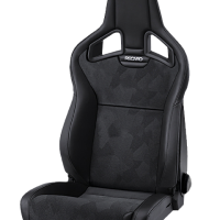 A black Recaro racing seat with adjustable components rests against a plain background. The seat features a high back, integrated headrest, and patterned fabric upholstery with ergonomic contours.
