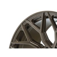 A close-up of a metallic car wheel rim showcases a geometric spoke design. The brand name "VOSSEN" is engraved near the edge. The background is plain white.