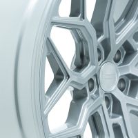 A close-up of a metallic alloy wheel with intricate geometric spokes. The center cap features embossed text: "VOSSEN" at the center, surrounded by "HYBRID FORGED." The background is plain and light.
