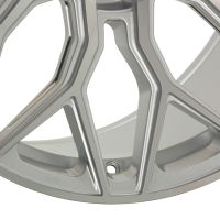 A metallic car wheel rim displays a complex geometric spoke design, positioned against a plain white background.