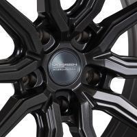 A dark, intricately designed wheel rim features a central hub cap with "VOSSEN HYBRID FORGED" text, surrounded by sharp, angular spokes against a plain white background.