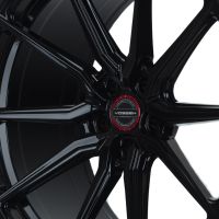 A black alloy wheel with a multi-spoke design features the text “VOSSEN FORGED” on the center cap. It is displayed against a white background.