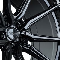 A shiny black alloy wheel with multiple spokes and a center cap displaying "Vossen Hybrid Forged," photographed in a close-up angle, highlighting its reflective surface and intricate design.