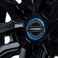 A black car wheel rim displays a center cap with blue and silver accents, featuring the text “VOSSEN HYBRID-FORGED,” “VOSSEN WHEELS,” “EST 2006 USA,” “PASSION · PERFORMANCE · PRECISION.”