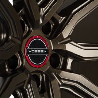 A bronze alloy wheel with a dynamic, multi-spoke design features a circular center cap displaying the text "VOSSEN" against a black and red background.
