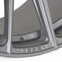 A metallic car wheel rim sits stationary, displaying a sleek, polished surface with the text "VOSSEN" engraved near its edge in a bright studio setting.