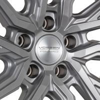 A metallic alloy wheel has intricate, angular spokes radiating from a central hub. Text on the hub reads: "VOSSEN HYBRID FORGED," showcasing the design's precision and branding.