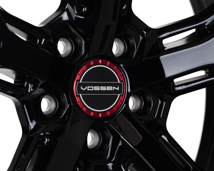 A glossy black alloy wheel with a central cap featuring the text "VOSSEN" in white, set against a red and black circular background.