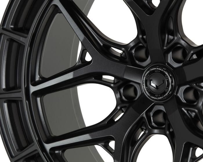 A black alloy wheel with intricate spoke design is displayed close-up against a white background. The central hub reads: "VOSSEN FORGED – ENGINEERED FORGED – VOSSEN WHEELS."