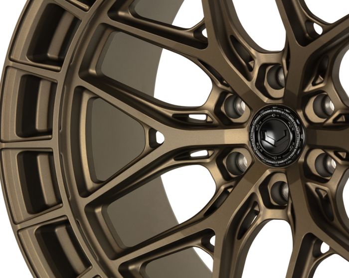 A bronze-colored alloy wheel displays intricate, multi-spoke design; a central cap features branding: "VOSSEN FORGED • VOSSEN WHEELS • T: MIAMI • L: USA • VOSSENFORGED.COM." The background is neutral.