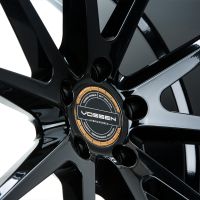 A glossy black wheel rim with multiple spokes displays "VOSSEN HYBRID FORGED" in the center. Surrounding text reads "VOSSEN WHEELS EST 2006 U.S.A." and "PASSION • PERFORMANCE • PRECISION".