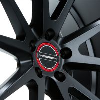 Black alloy wheel with a star-shaped pattern, centered on a red ring displaying the text "VOSSEN." The wheel is positioned against a neutral, light background.