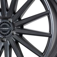 A glossy, dark gunmetal alloy wheel with multi-spoke design features the text "VOSSEN HYBRID FORGED," surrounded by "VOSSEN WHEELS EST 2006 USA" and "PASSION – PERFORMANCE – PRECISION" at the center.
