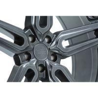 A metallic car wheel rim features intricate spoke design, focusing on the central hub with text: "VOSSEN HYBRID FORGED." It is in a bright, neutral setting.