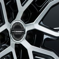 A metallic car wheel with a sleek, multi-spoke design features a central emblem reading, "VOSSEN HYBRID FORGED," surrounded by text: "VOSSEN WHEELS," "ESTP 2006 USA," "PASSION - PERFORMANCE - PRECISION."