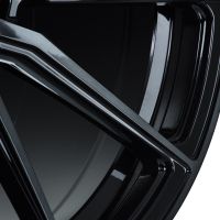 Close-up of a glossy black alloy wheel with angular spokes, reflecting light in a studio setting.