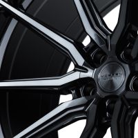 A glossy black alloy wheel features intricate spoke design and the text "Vossen Hybrid Forged" at the center, amidst a shadowed background.