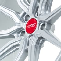 Silver alloy wheel featuring a multi-spoke design, with a red center cap displaying the text "Vossen Hybrid Forged," set against a plain, light background.