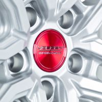 Silver alloy wheel rim featuring a red center cap with the text "VOSSEN HYBRID FORGED" embossed, highlighting intricate spokes and metallic texture.
