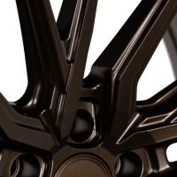Bronze metallic wheel rim with angular, intricate spokes converging at the center, reflecting light, set against a neutral background.