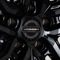 A detailed black wheel rim features the Vossen logo, with text: "VOSSEN WHEELS EST'D 2006 U.S.A HYBRID FORGED PASSION · PERFORMANCE · PRECISION," amidst glossy, angular spokes.
