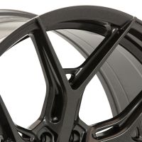 A close-up of a metallic, dark-colored car wheel rim with intricate, angular spoke design. The background is a neutral, light shade, highlighting the rim's sleek contours.