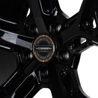 A glossy black alloy wheel features a central logo with text: "VOSSEN HYBRID FORGED, VOSSEN WHEELS EST 2006 U.S.A, FREEDOM · PERFORMANCE · PRECISION," set against a shiny metal background.