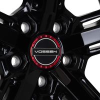 A glossy black alloy wheel features the logo "VOSSEN" at its center, bordered by a red ring, within a studio-lit environment.