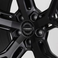 A black alloy wheel with a five-spoke design, centered on a hubcap labeled "Vossen Hybrid Forged," surrounded by text: "Vossen Wheels Est. 2006 U.S.A. Passion • Performance • Precision."