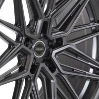 A metallic car rim with intricate, angular spokes extends radially, displayed against a plain backdrop. The central hub features text: “VOSSEN FORGED HYBRIDFORGED VOSSEN PERFORMANCE."