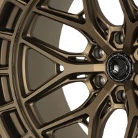 A bronze-colored, intricately designed car wheel rim with a central emblem, "Vossen Forged," is resting in a neutral setting. The text around the emblem reads, "VOSSEN WHEELS | FORGED | ENGINEERED ART."