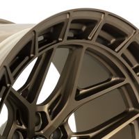 A metallic, bronze-colored car wheel rim with intricate spoke design sits against a plain background, showcasing its detailed craftsmanship and shiny finish.