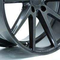 A dark, glossy car wheel rim has multiple spokes and is photographed against a plain white background. "VOSSEN" is engraved on the edge.