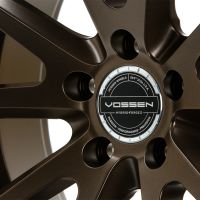 A dark brown metallic wheel rim, embellished with the logo "VOSSEN HYBRID FORGED" centered amidst sleek spokes. Text includes "VOSSEN WHEELS, EST 2006 USA, PASSION - PERFORMANCE - PRECISION."