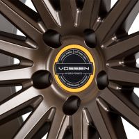 A bronze alloy wheel features multiple spokes radiating from a central hub. The hub displays text: "VOSSEN," "HYBRID-FORGED," "VOSSEN WHEELS," "EST 2006 U.S.A," "PASSION - PERFORMANCE - PRECISION."