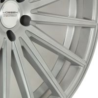 A silver alloy wheel with multiple thin spokes radiates outward, set against a plain background. The center features a logo with text: "VOSSEN HYBRID FORGED."